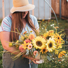 Load image into Gallery viewer, Bellingham florist holding large sunflower arrangement in yellow, peach and gold with textural elements