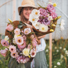 Load image into Gallery viewer, Laura holding large and medium bouquets with a light pink, white, and yellow color scheme of summer flowers (zinnias, cosmos, lisianthus, dahlias, and other blooms)