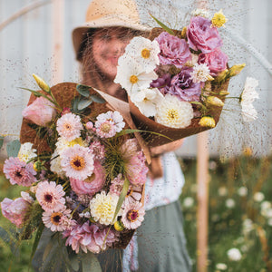 Laura holding large and medium bouquets with a light pink, white, and yellow color scheme of summer flowers (zinnias, cosmos, lisianthus, dahlias, and other blooms)